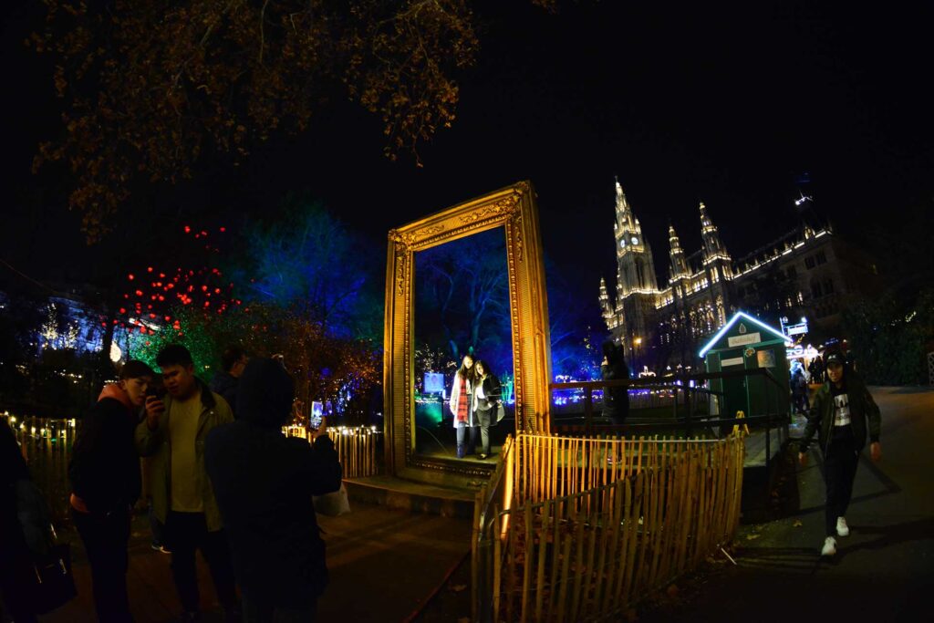 Interaktive Lichtinstallation Stadtplatz – Besucher vor einem beleuchteten, goldenen Bilderrahmen im Freien.
