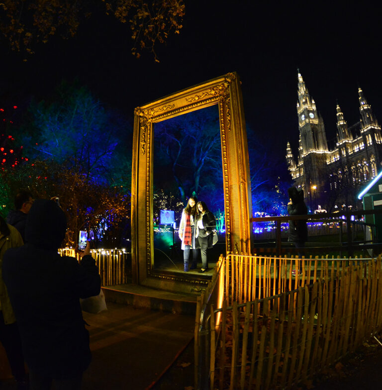 Interaktive Lichtinstallation Stadtplatz – Besucher vor einem beleuchteten, goldenen Bilderrahmen im Freien.