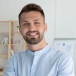 Porträt Mann 1 – Lächelnder Mann mit Bart in hellblauem Hemd im Büro.